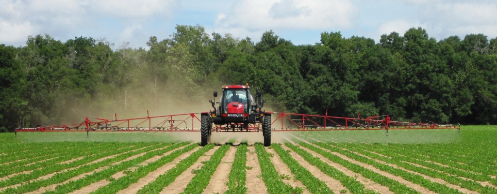 A tractor sprays pesticides over a field.